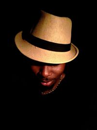 Close-up portrait of man wearing hat against black background