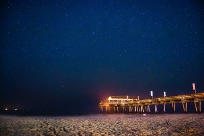 Illuminated pier on shore at beach against sky