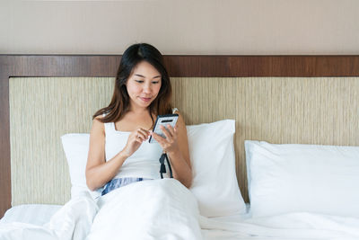 Young woman using mobile phone while sitting on bed