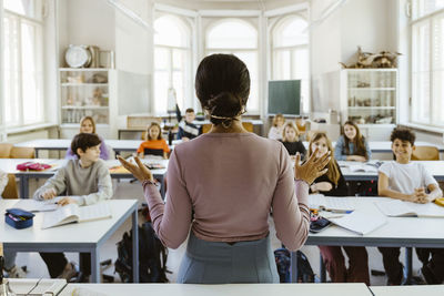 Rear view of female teacher explaining students sitting in classroom