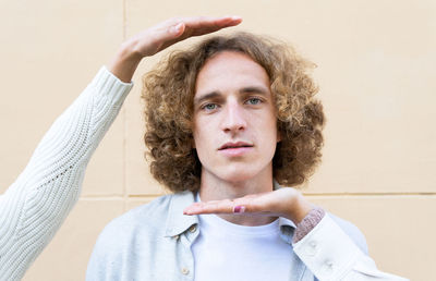 Crop female hands framing face of young man with curly hair looking calmly at camera