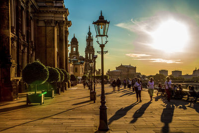 People on street by buildings in city during sunset