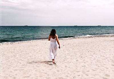 Rear view of woman walking on beach against sky during sunny day