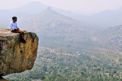 Man sitting on cliff over landscape