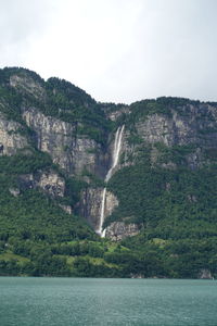 Scenic view of sea by mountain against sky