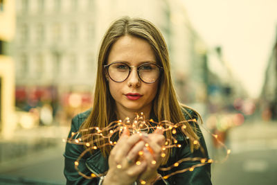 Close-up of young woman holding illuminated string lights