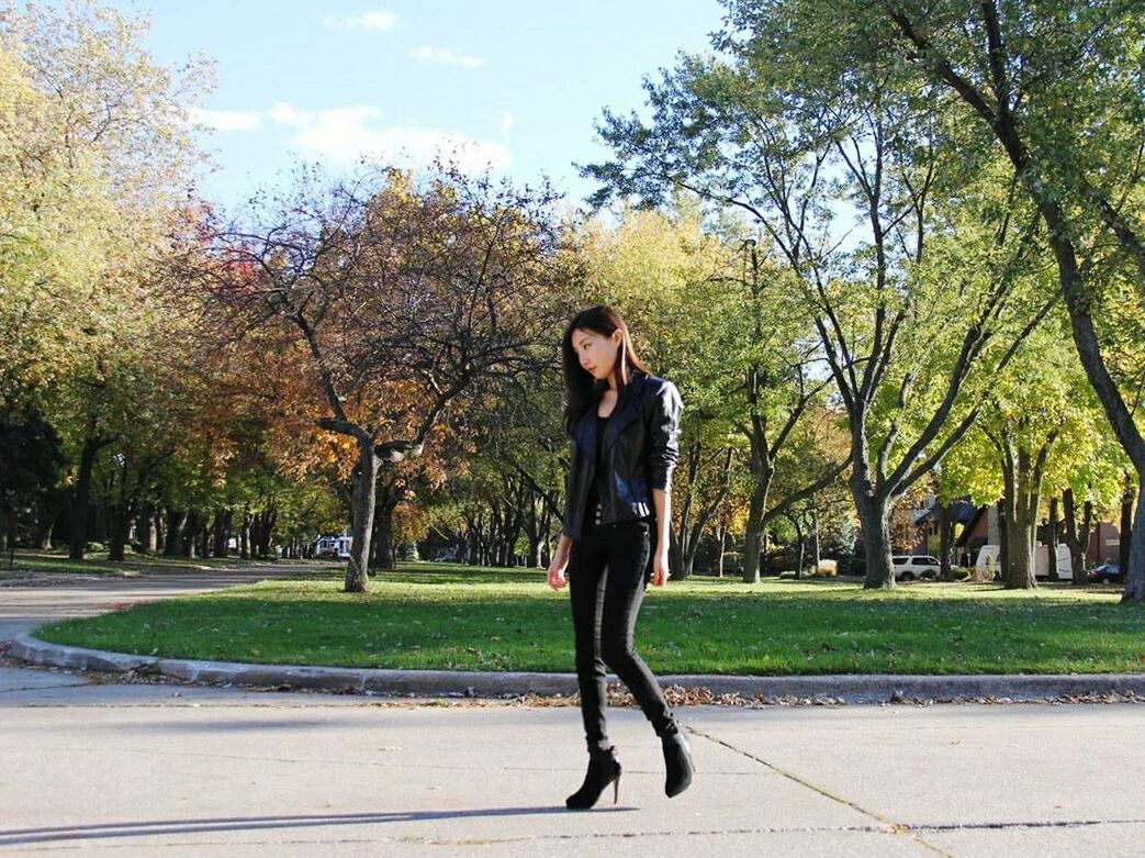 tree, lifestyles, casual clothing, full length, young adult, person, leisure activity, standing, young women, front view, road, park - man made space, sunlight, street, looking at camera, day, sky, portrait