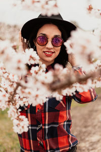 Portrait of woman wearing sunglasses and hat amidst pink flowers