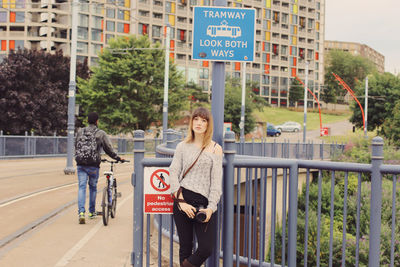 Portrait of woman holding camera while leaning on road sign