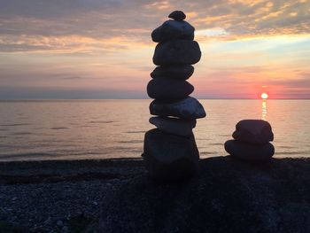 Stack of pebbles on beach against sky during sunset