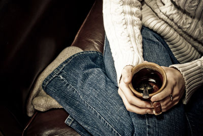 Low section of woman with coffee cup sitting on couch