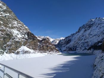 Scenic view of frozen lake and snowcapped mountains against clear blue sky