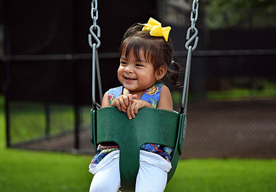 Girl looking away while sitting on swing in playground