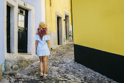 Rear view of young woman walking at alley amidst buildings