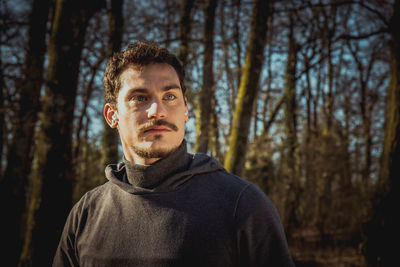 Runner is listening to the music while he stretches in the woods. 