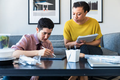 Businesswoman looking at male colleague using graphics tablet while sitting at table in office