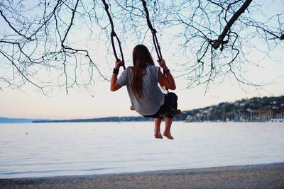 Full length rear view of woman swinging on swing at lakeshore