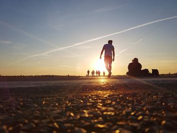 Silhouette people on beach against sky during sunset