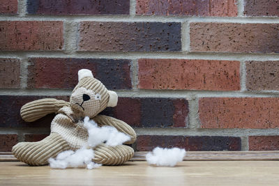 Close-up of torn stuffed toy on wooden table by brick wall