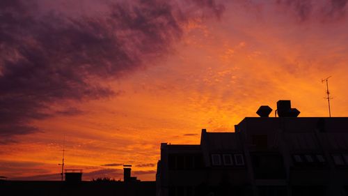 Low angle view of silhouette buildings against orange sky