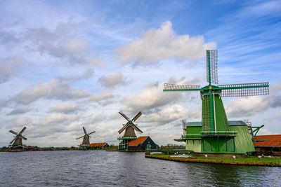 Traditional windmill by river against sky