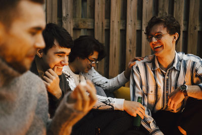 Happy young male friends talking while spending leisure time in balcony