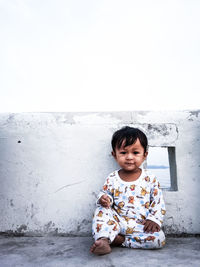 Portrait of smiling baby boy sitting against wall