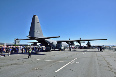 People at airport runway against clear blue sky