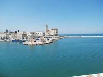 Buildings by sea against clear blue sky