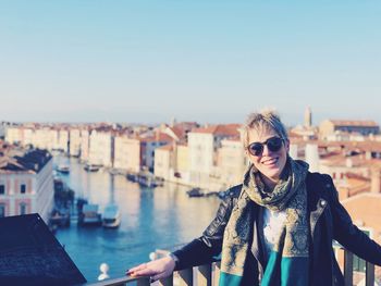Portrait of cheerful woman wearing sunglasses while standing against river in city