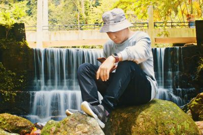 Man sitting on rock by waterfall