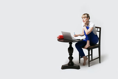 Young woman using laptop while sitting against white background