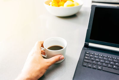 Midsection of person holding coffee cup and laptop on table