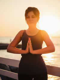 Portrait of woman doing yoga against sea during sunrise