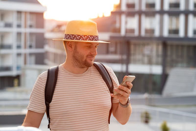 Handsome adult blond bearded man wearing sunhat using cellphone, mobile, texting, chatting