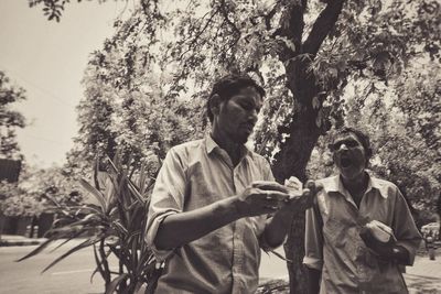 Young man using mobile phone against trees