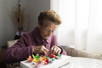 Senior woman making craft sitting at dining table