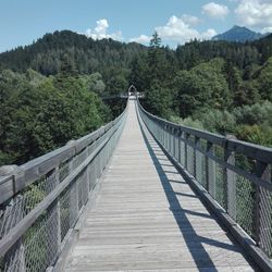 Footbridge amidst trees in forest against sky