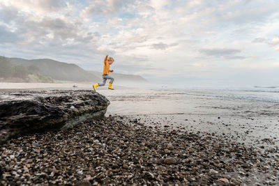 Young curly haired child leaping from rock at beach in new zealand