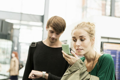 Man looking at time while friend applying make-up at railroad station