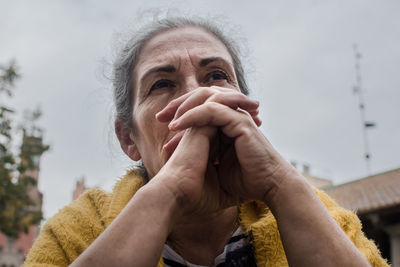 Low angle view of woman with hands clasped sitting outdoors