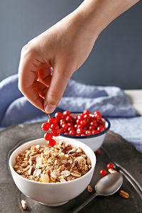 Cropped image of hand holding red current over oatmeal on table