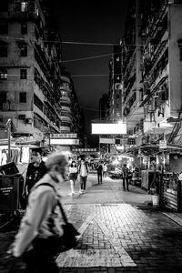 People walking on street against illuminated buildings in city