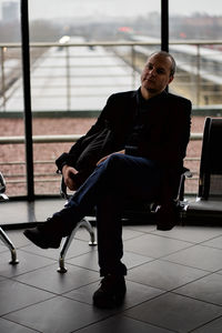 Young man sitting on chair against glass window