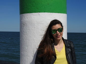 Portrait of woman wearing sunglasses by column against sea