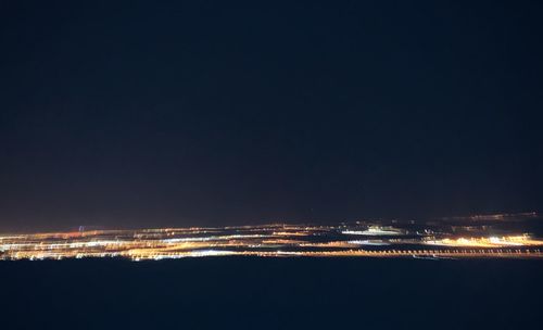 Illuminated city by sea against clear sky at night