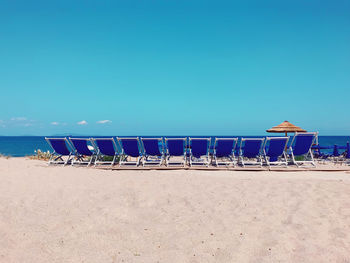 Chairs on beach against clear blue sky