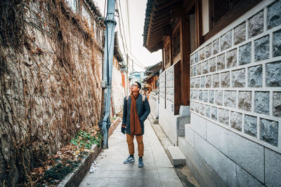 Full length of woman walking on footpath amidst buildings in city