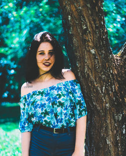 Portrait of smiling young woman standing against tree trunk