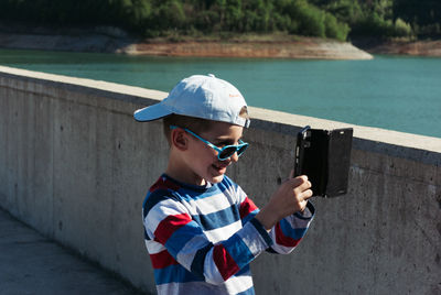 Smiling boy photographing while standing on bridge